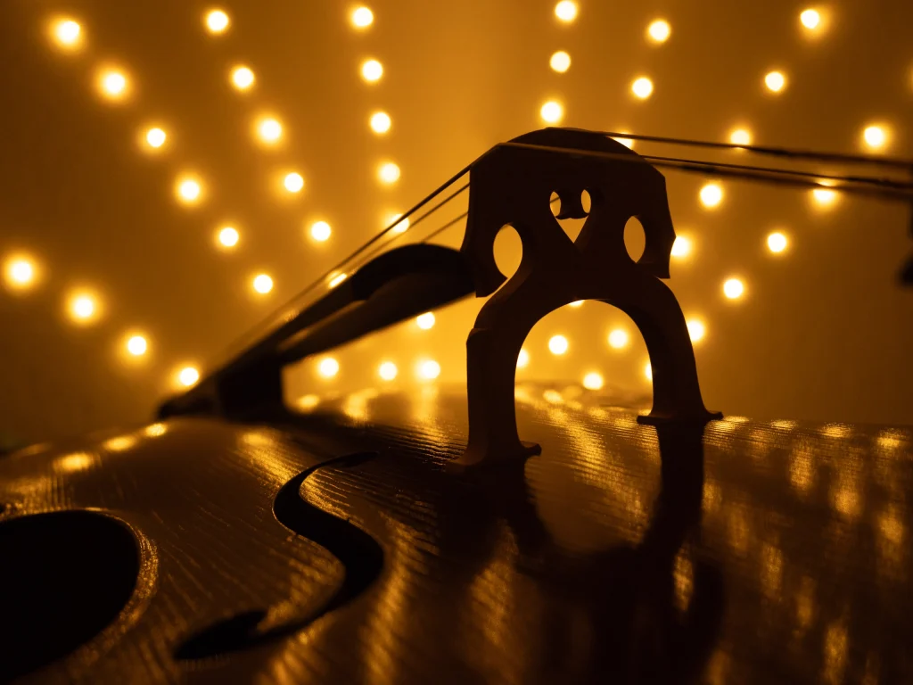 Im Hintergrund eine strahlenförmige Lichterkette, die warmes Licht gibt und im Vordergrund die Silhouette eines Cellos erkennen lässt